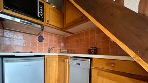 A compact kitchen with wooden cabinets, a microwave, a dishwasher, and a tiled backsplash. - Mini T2 Duplex in Barcelonnette, perfect for 4 (Barcelonnette)