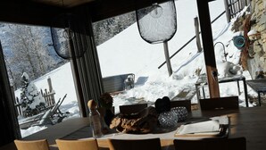 A wooden dining table with chairs, a view of a snowy landscape, and a stone wall. - Holiday Home "Bergsuite" with Mountain View, Balcony, Garden & Wi-Fi (St.Martin in Passeier)
