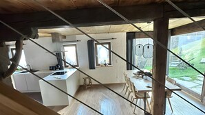 A modern kitchen with wooden beams, a dining area with a table and chairs, and large windows offering a view of the outdoors. - Holiday Home "Bergsuite" with Mountain View, Balcony, Garden & Wi-Fi (St.Martin in Passeier)