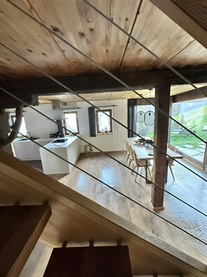 A modern kitchen with wooden beams, a dining area with a table and chairs, and large windows offering a view of the outdoors.