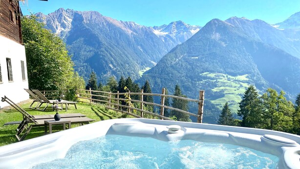 A hot tub with a mountain view, wooden deck chairs, and a wooden fence. - Holiday Home "Bergsuite" with Mountain View, Balcony, Garden & Wi-Fi (St.Martin in Passeier)