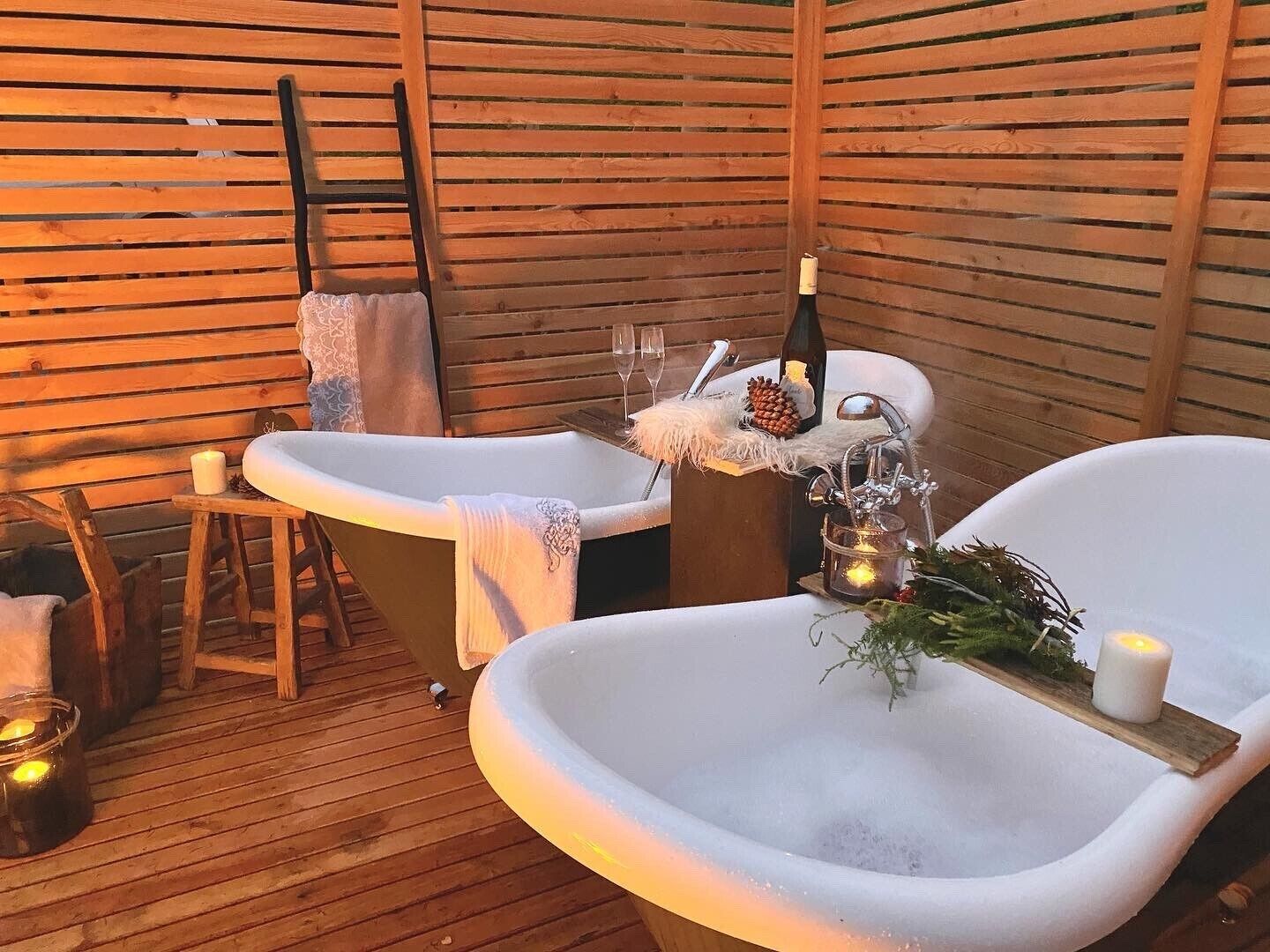 A wooden deck with two white tubs, a bottle of champagne, and candles.