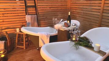 A wooden deck with two white tubs, a bottle of champagne, and candles.