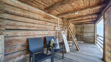 A wooden cabin interior with a wooden floor, a bench, a ladder, and a window overlooking a mountainous landscape.