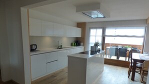 Une cuisine moderne avec des meubles blancs, un îlot central et un coin repas doté de meubles en bois.