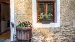 A rustic stone wall with a wooden barrel planter and a window with wooden shutters. - Apartment “Schildhofsuite” in “Schildhof Ebion” with Mountain View & Garden (St. Leonhard Passeier)