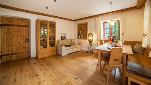 A cozy room with wooden floors, a sofa, a dining table with chairs, a lamp, and a window with curtains. - Apartment “Schildhofsuite” in “Schildhof Ebion” with Mountain View & Garden (St. Leonhard Passeier)