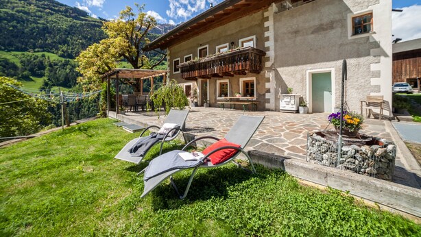 A chalet with a stone terrace, outdoor seating, and a view of a mountainous landscape. - Apartment “Schildhofsuite” in “Schildhof Ebion” with Mountain View & Garden (St. Leonhard Passeier)