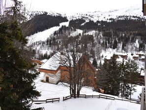 A snow-covered mountain landscape with a wooden cabin and a fenced area in the foreground.