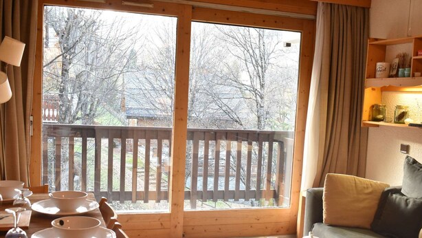 A cozy room with a wooden dining table set for tea, a sofa, and a view of a wooden deck and trees outside. - Ski-In/Ski-Out Studio for 4 in Méribel, Pool Access, Near Shops & Bus Stop (Méribel)