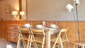 A dining area with a wooden table set for four, equipped with white plates, bowls, and cups. There are two floor lamps and a mirror on the wall. - Ski-In/Ski-Out Studio for 4 in Méribel, Pool Access, Near Shops & Bus Stop (Méribel)