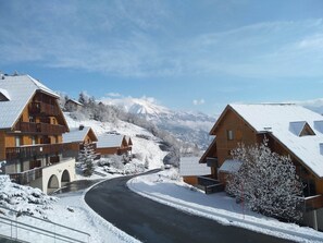 Un pueblo cubierto de nieve con casas de madera, un camino sinuoso y una vista despejada de montañas nevadas al fondo.