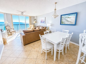 A spacious living area with a white dining table and chairs, a beige sofa, and a balcony with a view of the ocean. - Ashworth 603 (North Myrtle Beach)