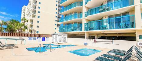 A hotel pool area with multiple swimming pools, sun loungers, and a lifeguard stand.