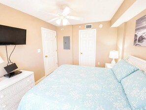 A bedroom with a bed, a television, a desk, and a ceiling fan.