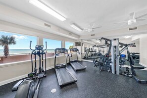 Un gimnasio con cintas de correr, elípticas y equipo de pesas, con vistas a una playa.