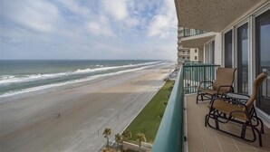 Un balcon avec vue sur la plage, un espace piscine et un immeuble à plusieurs étages.