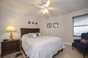Un dormitorio con una cama, una mesita de noche, una lámpara, una silla y un ventilador de techo.