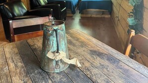 Een knus houten interieur met een houten tafel, een metalen kan, twee bedden en een televisie.