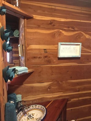 A wooden cabin interior with a sink, a towel rack, and a sign that reads 'wash up BUTTERCUP.'