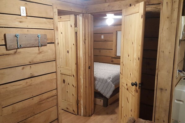A wooden-paneled room with a bed, a door, and a wall-mounted light fixture.
