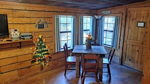 Een houten blokhut van binnen met een eettafel, stoelen, een kerstboom en een open haard.