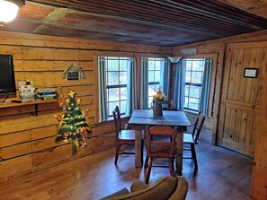 A wooden cabin interior with a dining table, chairs, a Christmas tree, and a fireplace.