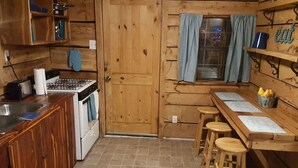Een houten keukentje met een fornuis, spoelbak en barstoelen.