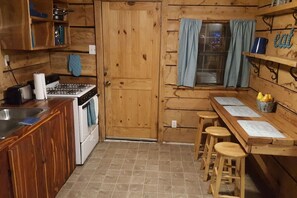 A wooden cabin kitchen with a stove, sink, and bar stools.