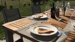 Uma mesa posta ao ar livre, com prato de comida, copos de vinho e garrafas.
