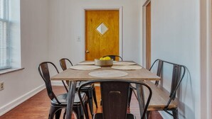 A dining area with a wooden table and metal chairs, a wooden door with a diamond-shaped mirror, and a window with blinds. - Stairway | 3BR Apt w W/D, Home Theater (Philadelphia)