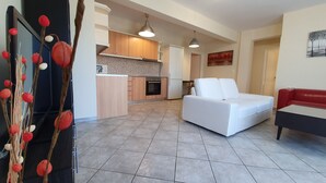 A modern living room with a white sofa, a red and white couch, and a kitchen area with wooden cabinets and a tiled backsplash. - MTC-SK Apartment by the sea and Airport  (Markopoulo Mesogaias)