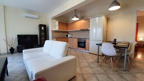 A modern living room with a white sofa, a flat-screen TV, and a dining area with a table and chairs. - MTC-SK Apartment by the sea and Airport  (Markopoulo Mesogaias)