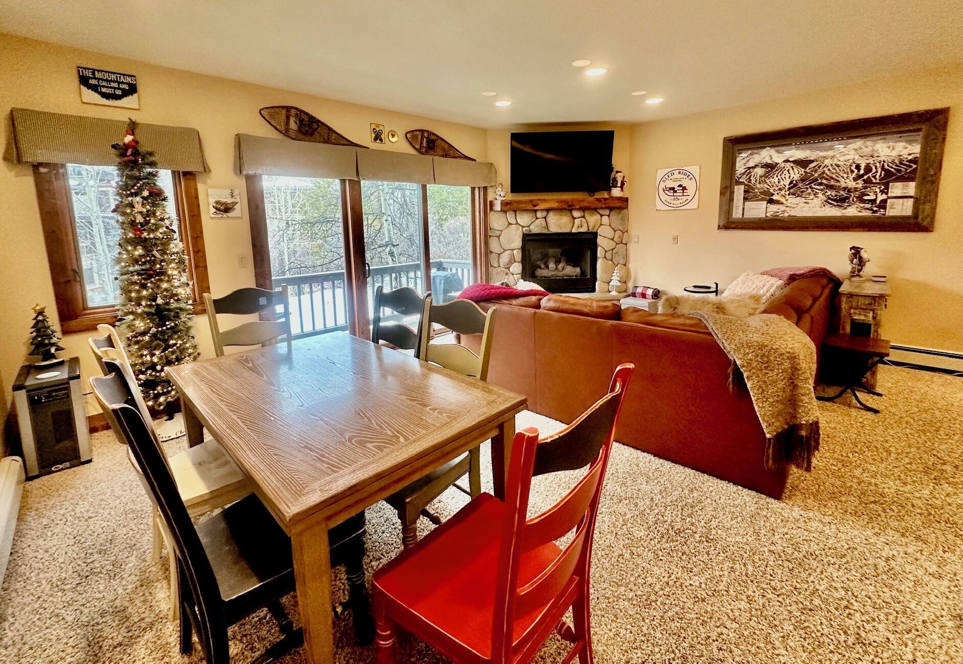 A cozy living room with a fireplace, a dining area with a wooden table and chairs, and a Christmas tree.