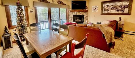 A cozy living room with a fireplace, a dining area with a wooden table and chairs, and a Christmas tree.