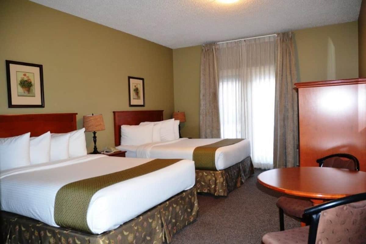 Une chambre d’hôtel avec deux lits, une petite table, une chaise et une fenêtre avec des rideaux.