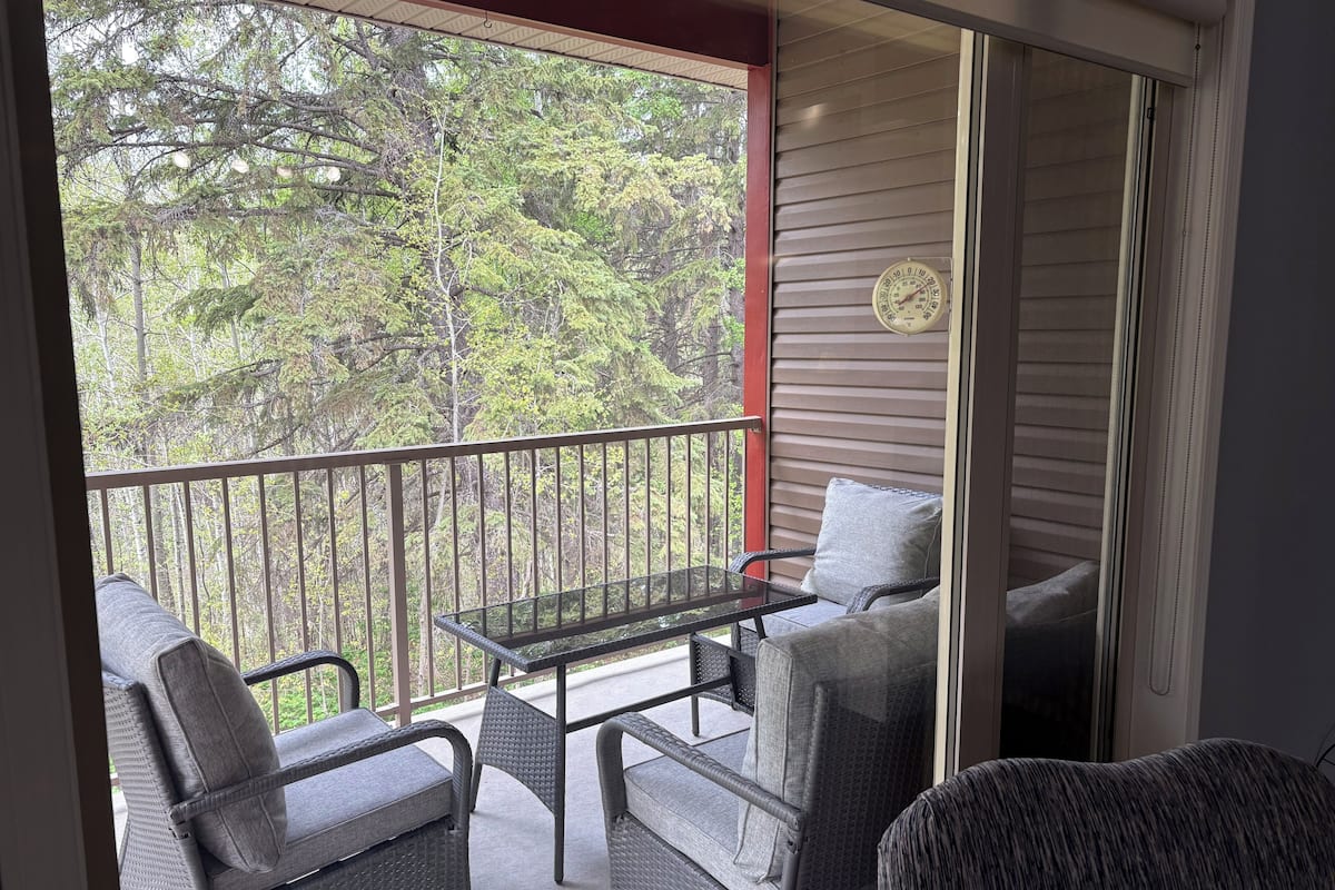 Un balcon agrémenté de meubles en osier, d’une table et offrant une vue sur les arbres.