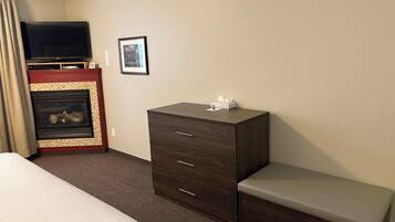 Una habitación de hotel con cama, cómoda, banco, chimenea y televisión.