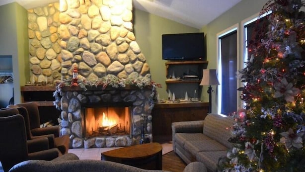 Ein gemütliches Wohnzimmer mit Kamin aus Stein, bequemen Sitzgelegenheiten, einem Weihnachtsbaum und einem Flachbildfernseher.