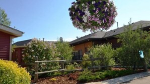 Ein hängender Blumenkorb mit verschiedenen Blumen, ein Holzzaun und ein Gebäude mit Satteldach.