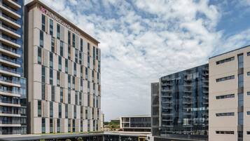 Un hôtel moderne, reconnaissable à son enseigne Hilton Garden Inn bien visible, qui se distingue par sa façade épurée et structurée et son espace extérieur abrité, aménagé avec des sièges.