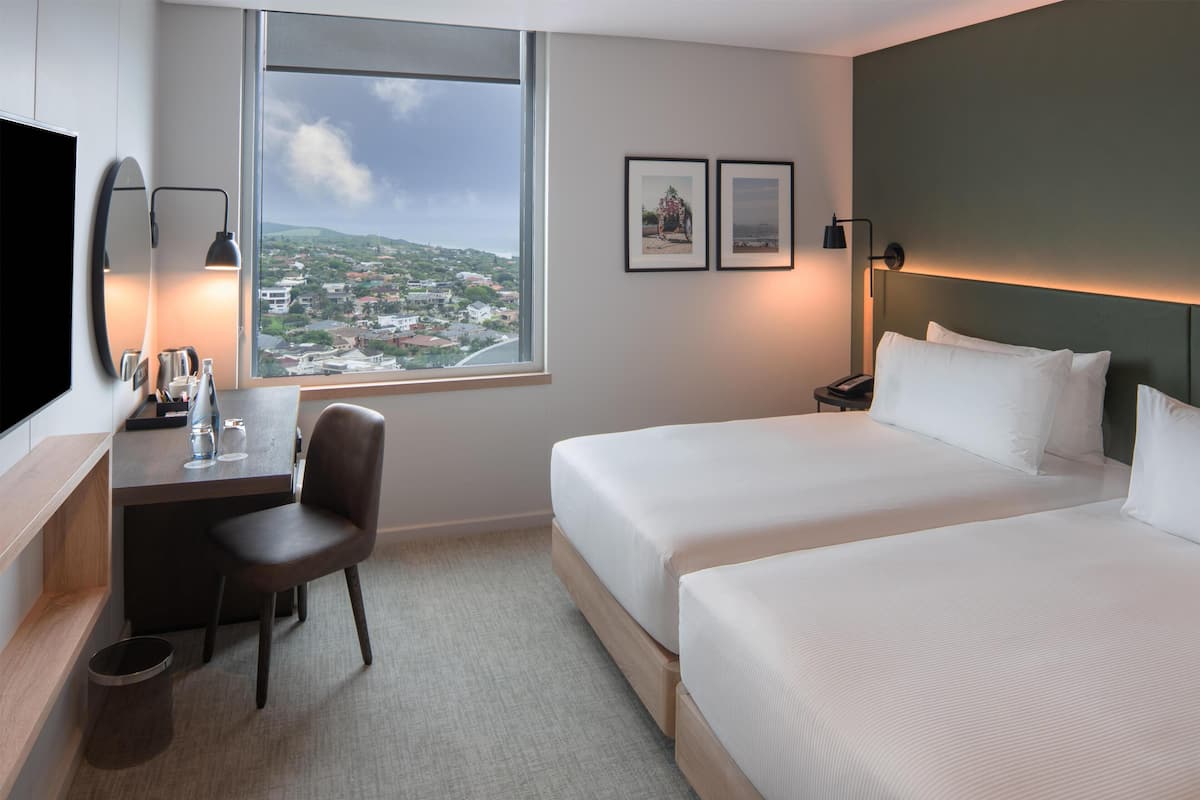 A hotel room with a bed, a desk with a chair, a TV, and a window with a view of a cityscape.