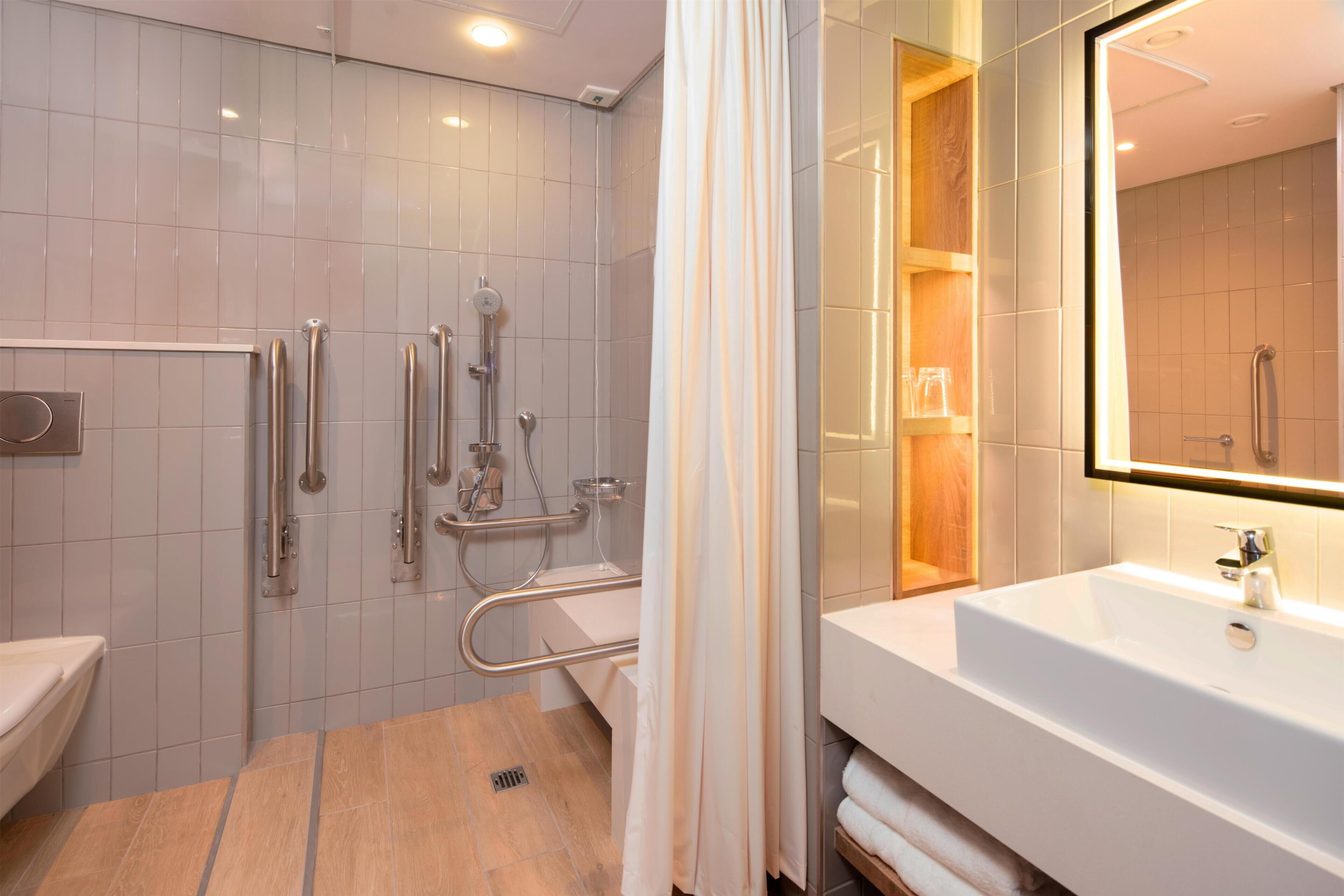 A modern bathroom with a shower, grab bars, a sink, and a mirror.