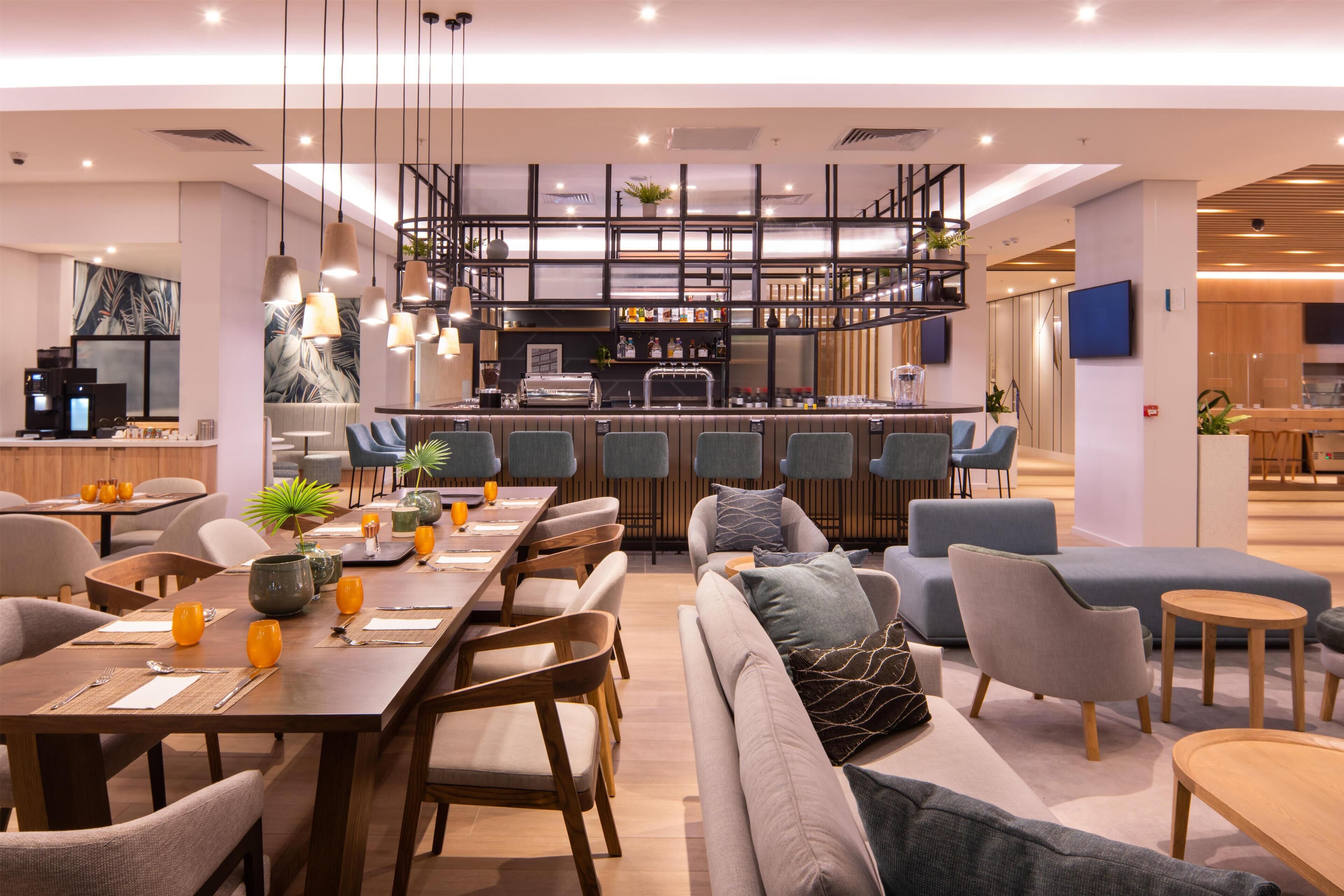 A modern hotel lobby with a dining area, seating arrangements, and a bar.