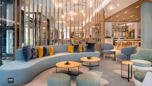A modern lounge area with a curved sofa, round tables, and a wooden partition with hanging lights. - Hilton Garden Inn Umhlanga Arch (Umhlanga)