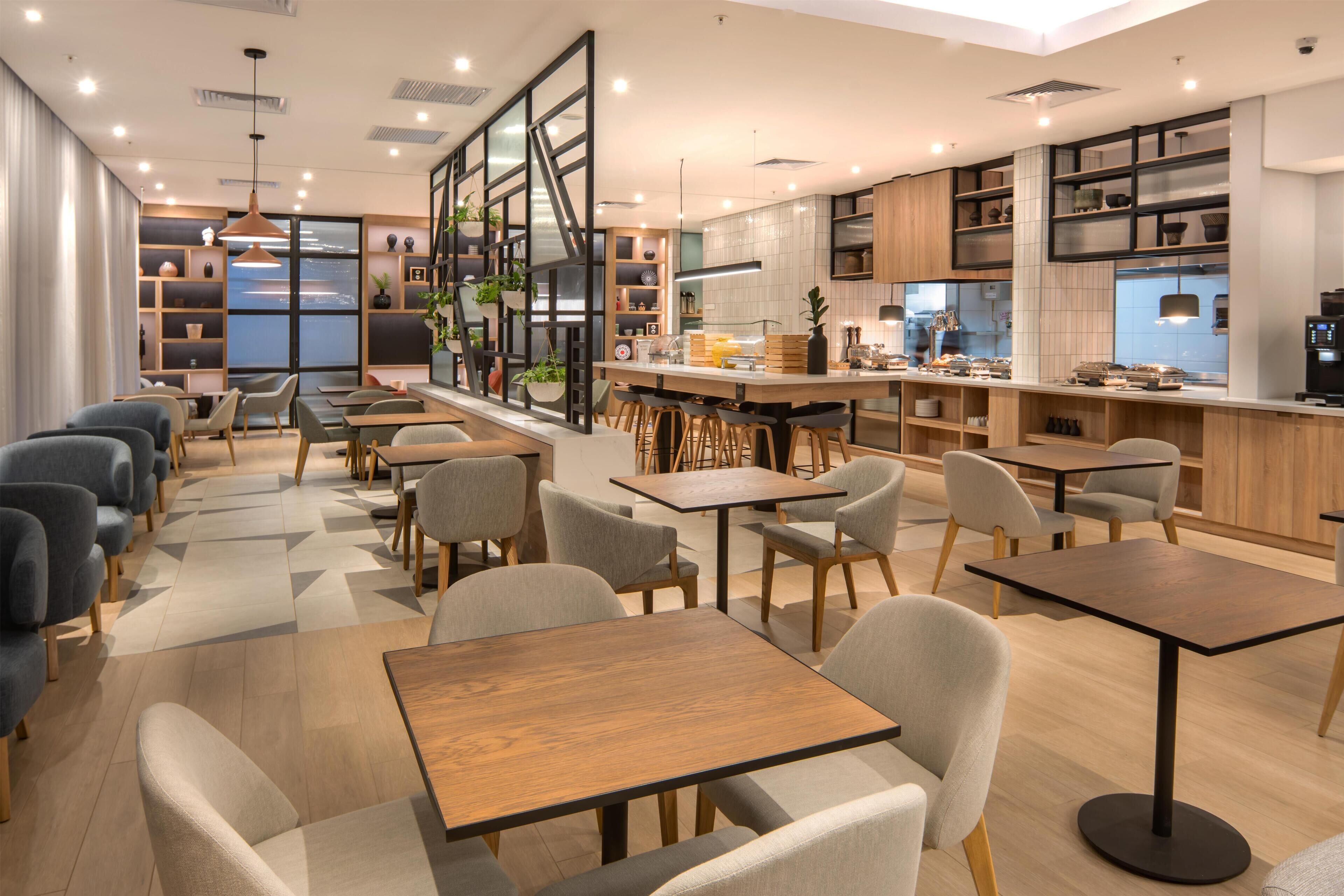 A modern restaurant interior with multiple seating areas, a bar, and a kitchen visible through the glass.