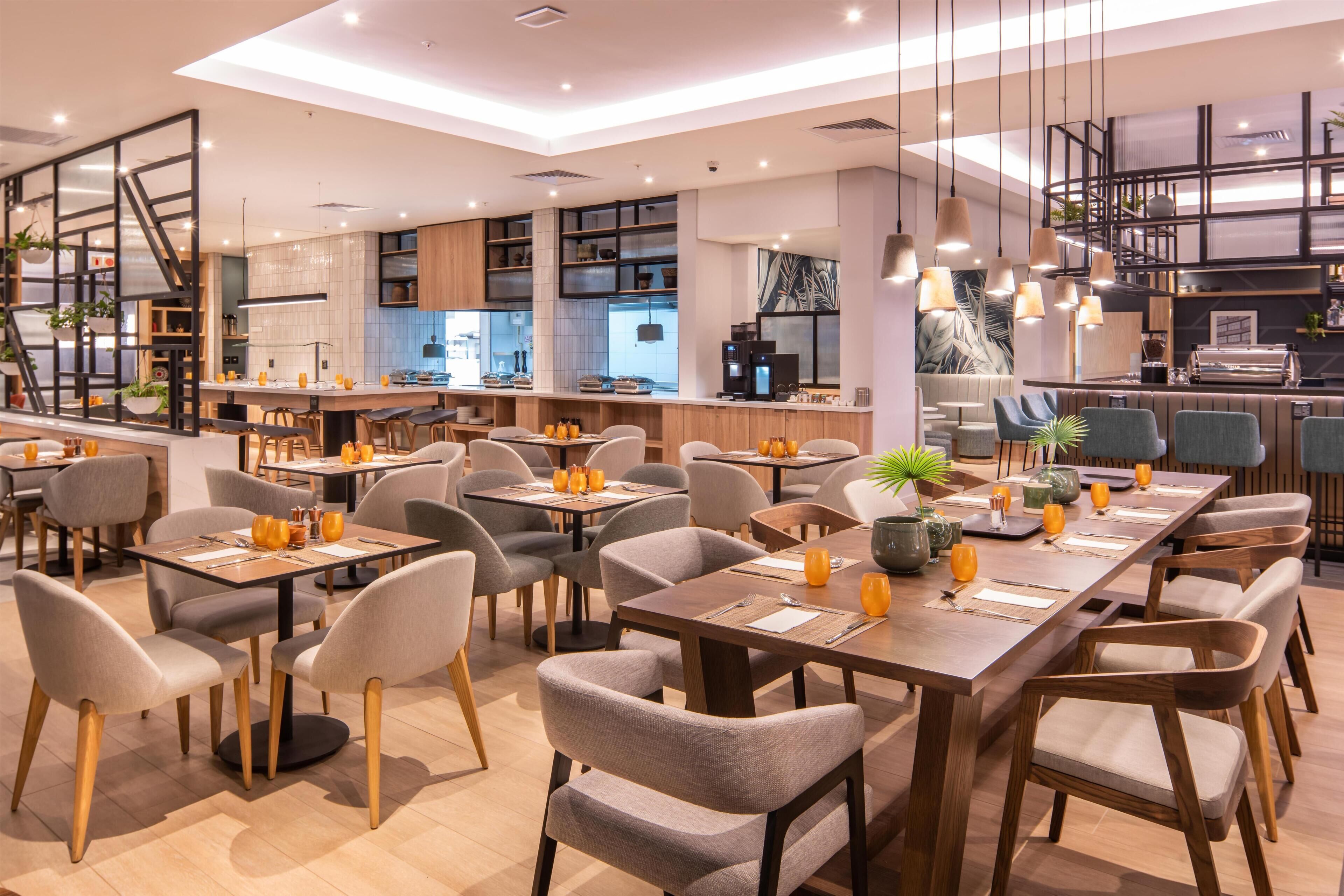 A modern restaurant with multiple dining tables, chairs, and a bar area.
