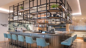 A modern bar area with a curved counter, bar stools, and shelves with bottles. - Hilton Garden Inn Umhlanga Arch (Umhlanga)