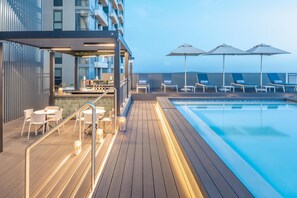 Un espace piscine aménagé sur le toit, avec des chaises longues, des parasols et un bar.