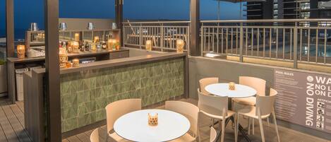 A rooftop bar with a pool view, bar area, and seating.
